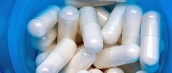 Medications in blue container. Close up of a pile of white capsules. Top view, high resolution product. Health care concept